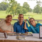 Group of three people sitting at the Teeing for abilities raffle table selling tickets and smiling